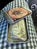 A cup of brewed blended tea with tea powder, a bamboo scoop and a bamboo whisk on a tray with some spilled tea powder in the tray.